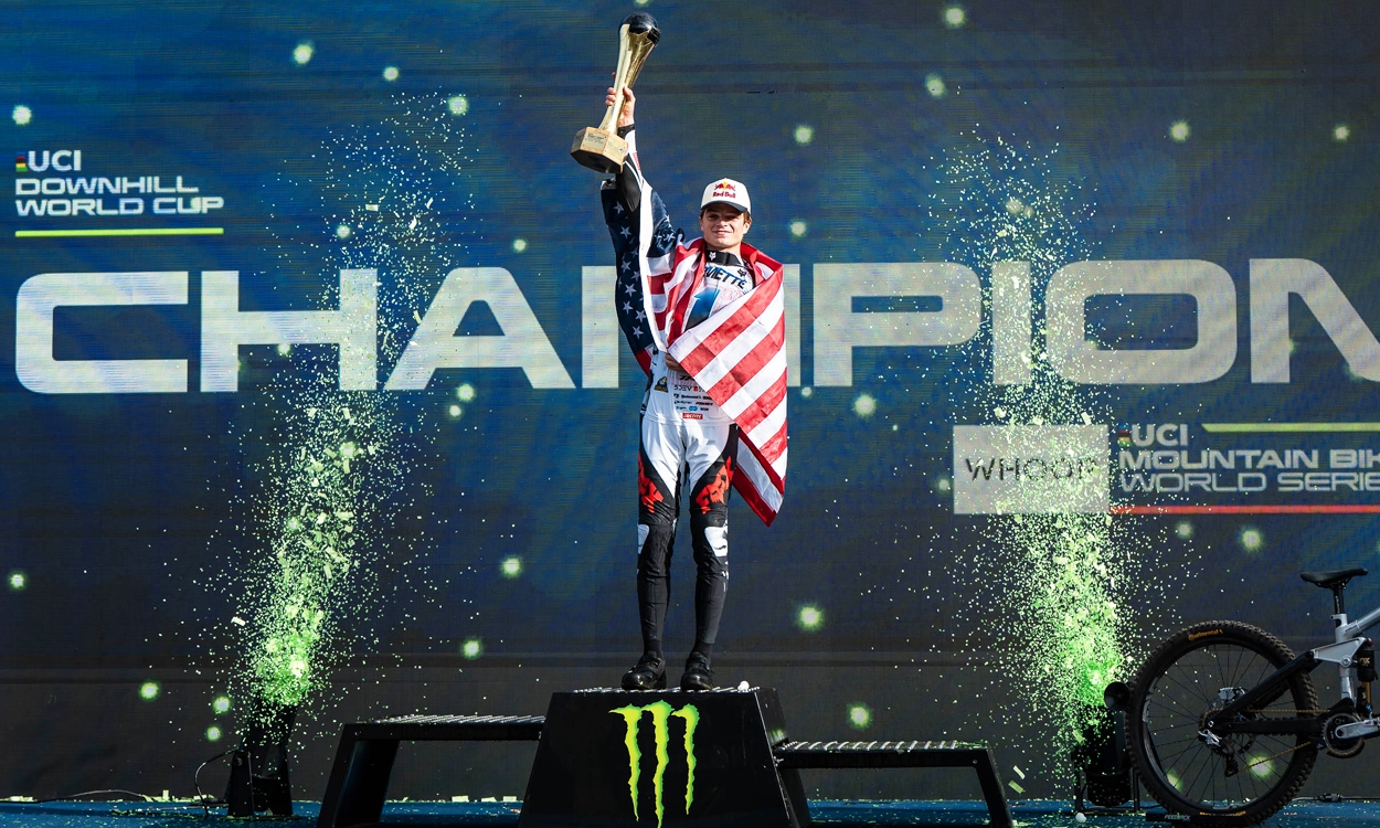 A pro mountain biker stands atop of the podium with a gold trophy